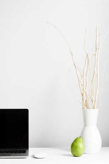 Composition of workplace with vase and laptop on desk