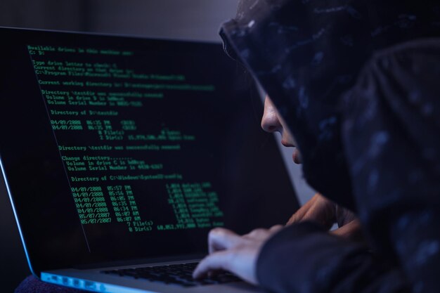 computer hacker in hooded shirt typing software algorithms and stealing data from computer network on laptop