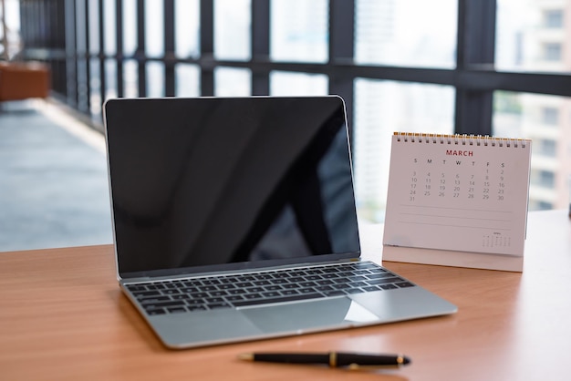 Компьютерный ноутбук с пустым черным экраном и календарем на столе в современном офисе