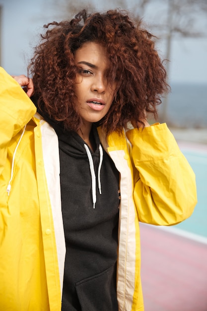 Concentrated african curly young woman wearing yellow coat