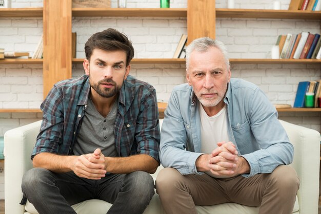 Concentrated aged man and young guy watching TV on sofa