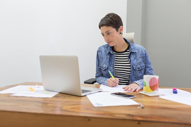 Free photo concentrated businesswoman looking at laptop and holding a pen