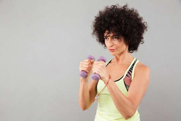 Concentrated curly fitness woman doing exercise with dumbbells