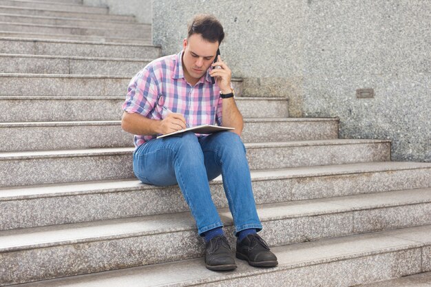 Concentrated freelancer making notes and talking on phone