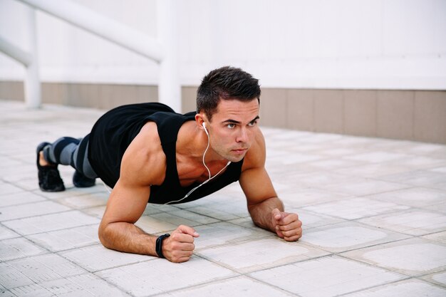 Concentrated handsome sportsman in earphones, doing push ups on elbows, working out