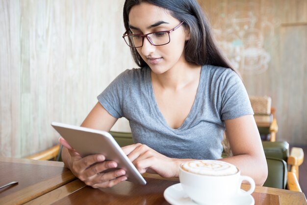 Концентрированный индийский студент, используя планшет в кафе
