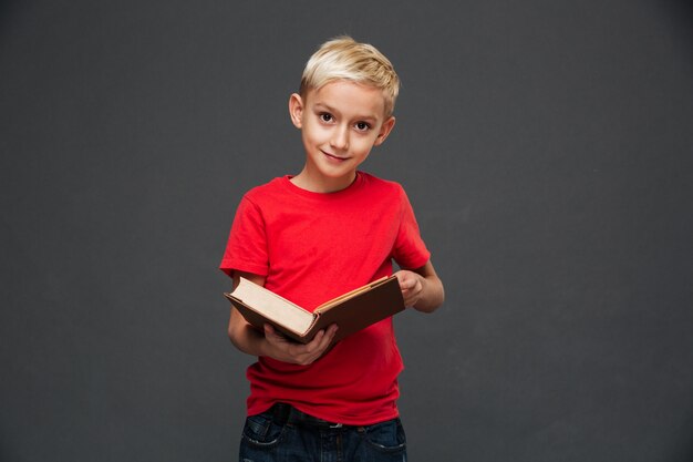 Сконцентрированный маленький мальчик держа книгу.