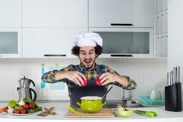 Concentrated male chef with fresh vegetables holding red peppers in the white kitchen