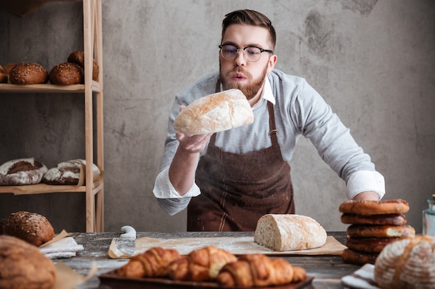 Concentrated man baker standing at bakery holding bread