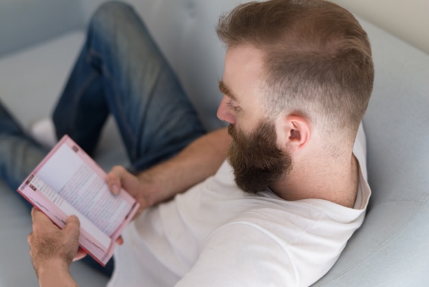 Foto gratuita l'uomo concentrato si è concentrato sul contenuto del libro che si siede sul sofà