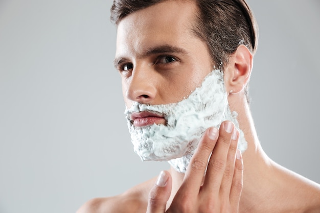 Concentrated man standing isolated with shaving foam on face