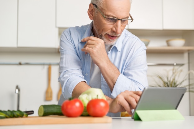 Vetri d'uso concentrati dell'uomo maturo che cucinano insalata