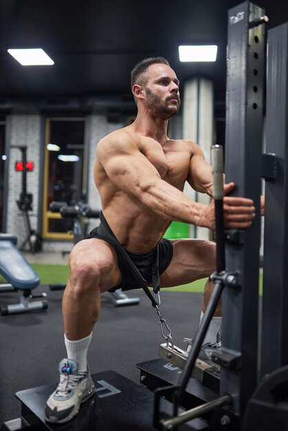 Concentrated muscular man in black shorts doing squats with weight training in modern gym low angle