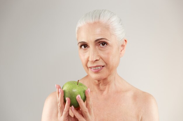 Сконцентрированная нагая пожилая женщина держа яблоко.