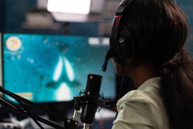 Concentrated pro gamer talking into microphone during live streaming while playing online video games during space shooter championship. Esport player using RBG computer equipment. E sport tournament