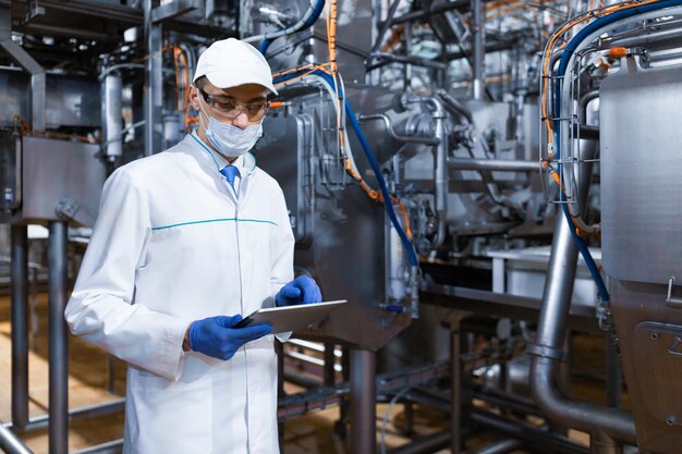 유제품 공장 검사관의 생산 부서에 서서 치즈 공장에서 제어를 수행하는 동안 디지털 태블릿의 도움으로 필요한 메모를 하는 집중된 기술자