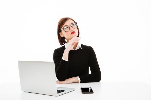 Сконцентрированная думая молодая бизнес-леди используя портативный компьютер