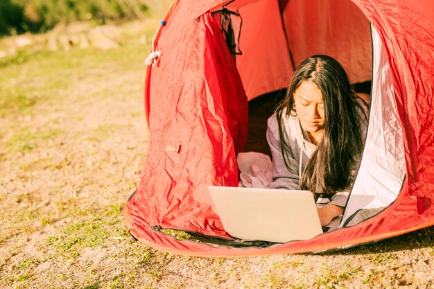 Concentrated woman using laptop lying in tent 