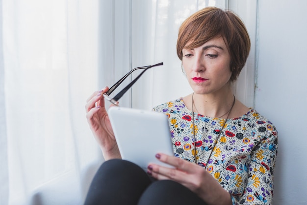 Concentrated woman with tablet and glasses in hands