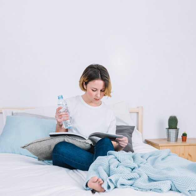 Concentrated woman with water reading magazine