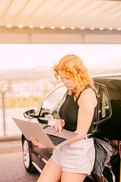 Concentrated woman working on laptop beside car