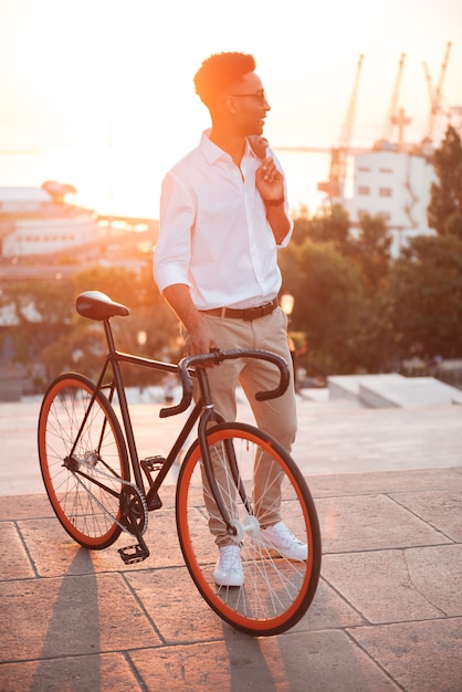 Сконцентрированный молодой африканский человек рано утром с велосипедом