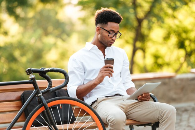 Concentrated young african man using tablet drinking coffee.