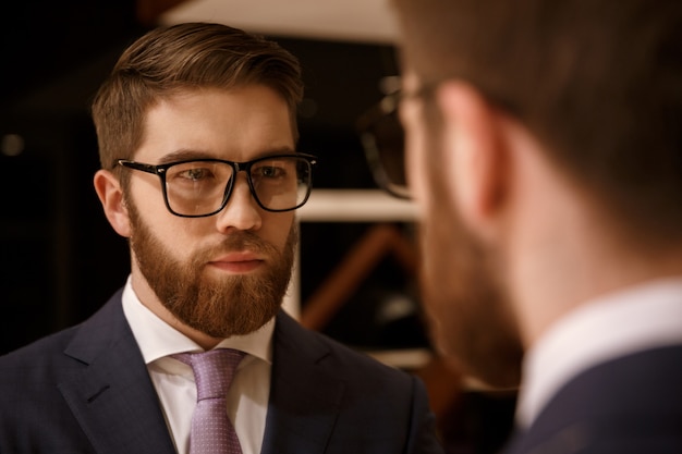 Free photo concentrated young bearded businessman looking at mirror