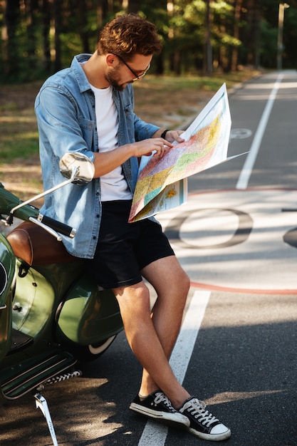 Concentrated young bearded man near scooter looking at map