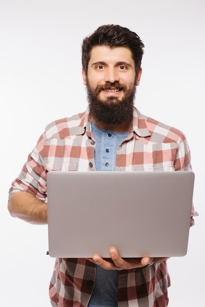 Concentrated young bearded man wearing glasses dressed in shirt using laptop isolated over white wall.