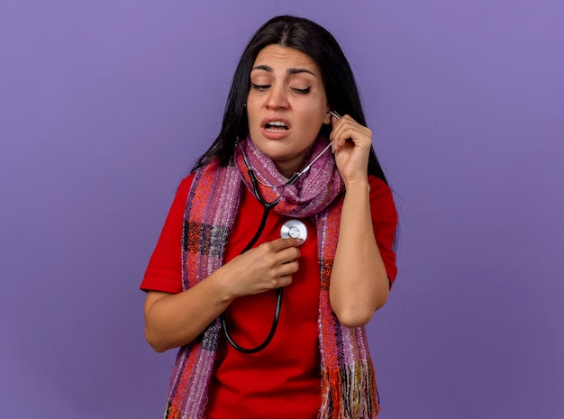 Free photo concentrated young caucasian ill girl wearing scarf and stethoscope looking at side listening to her heartbeat isolated on purple wall with copy space