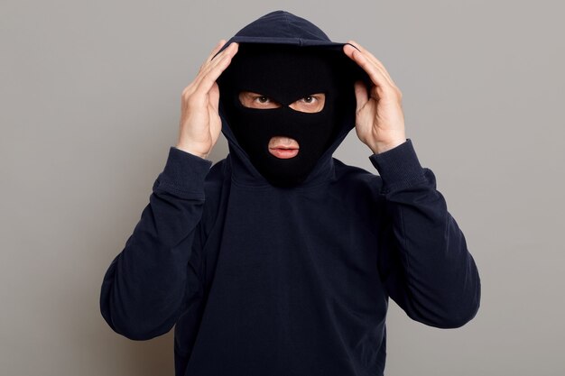Сосредоточенный молодой преступник в маске бандита с капюшоном