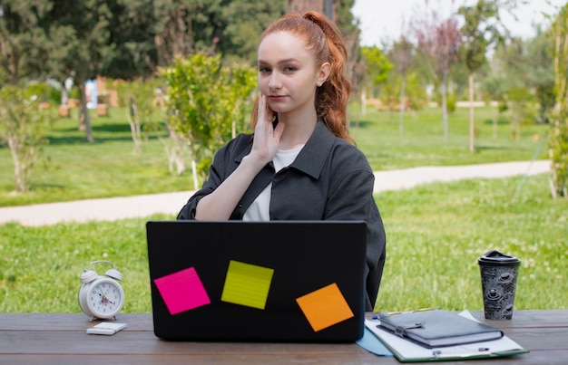 Concentrated young freelancer student working at laptop oudoors thinking