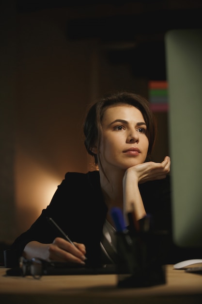 Concentrated young lady designer sitting in office at night