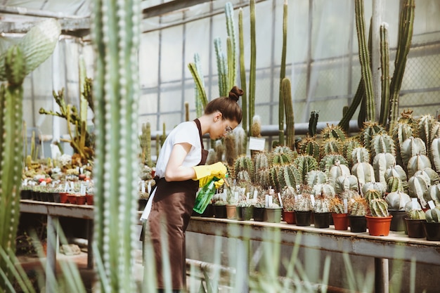 Free photo concentrated young lady in glasses standing in greenhouse