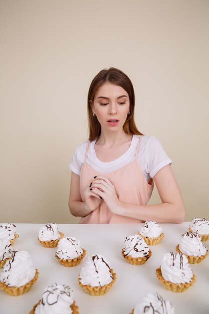 Концентрированная молодая леди сидит и позирует возле кексы