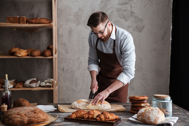 集中した若い男のパン屋がパンを切った。