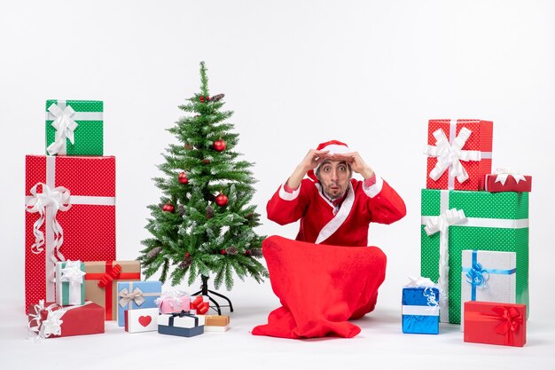 Concentrated young man celebrate new year or christmas holiday sitting on the ground near gifts and decorated Xmas tree