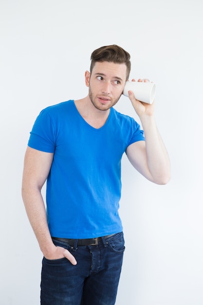 Concentrated young man eavesdropping with mug