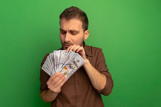 Сосредоточенный молодой человек держит и смотрит на деньги, считая их изолированными на зеленой стене