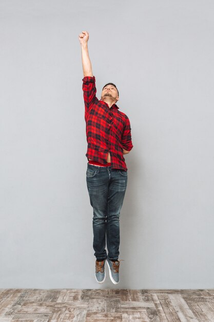 Concentrated young man jumping over grey wall.