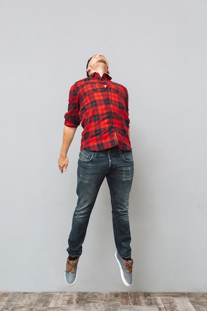 Concentrated young man jumping over grey wall.