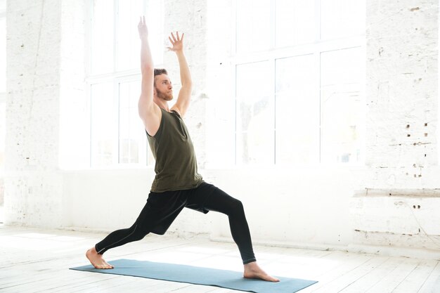 Concentrated young man parctising yoga pose on a fitness mat