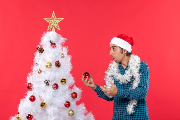 Concentrated young man with santa claus hat in a blue stripped shirt and holding decotaion accessory standing