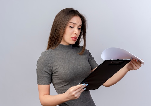 Concentrated young pretty woman holding and looking at clipboard isolated on white background