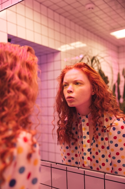 거울을보고 집중된 젊은 빨강 머리 곱슬 아가씨.