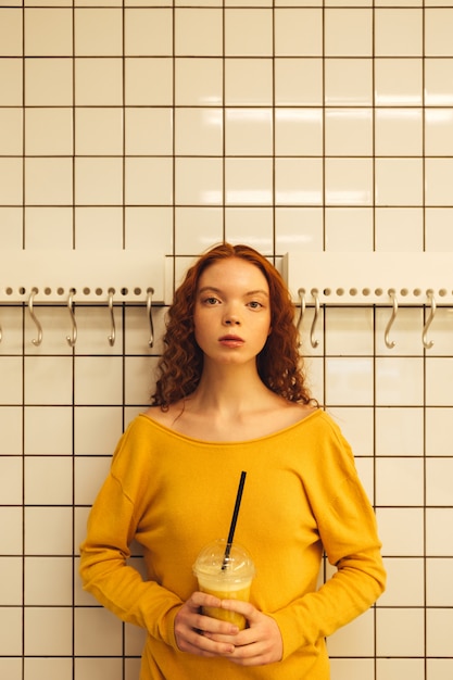 Free photo concentrated young redhead curly lady standing in cafe