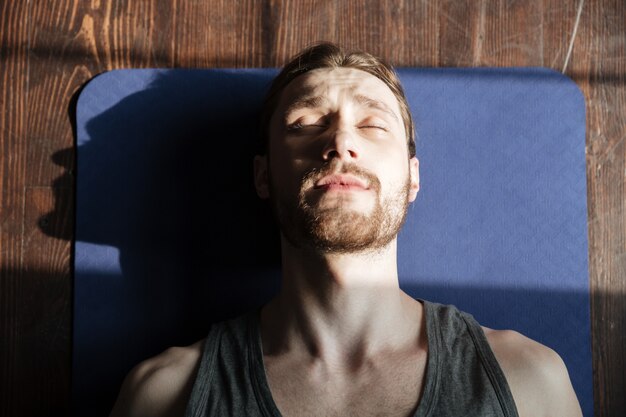 Concentrated young strong sportsman in gym lies on floor