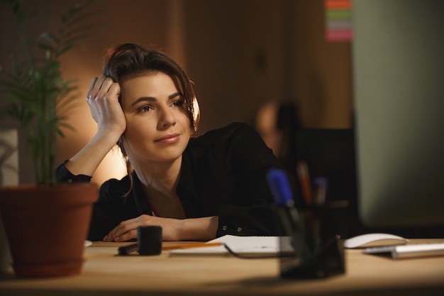 Сконцентрированный дизайнер молодой женщины сидя в офисе на ноче