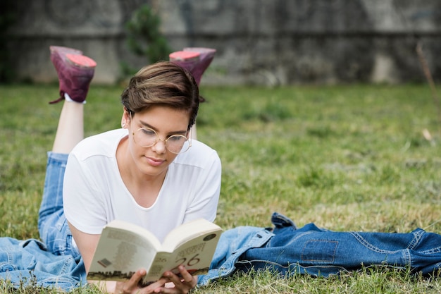 Концентрированная молодая женщина, чтение лежа на газоне